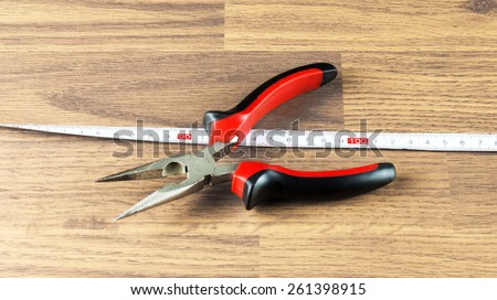 Pliers and measuring tape on the background Wooden floor