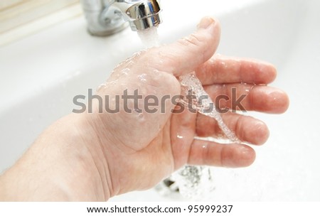 Washing of hands under the crane with water against a white washstand