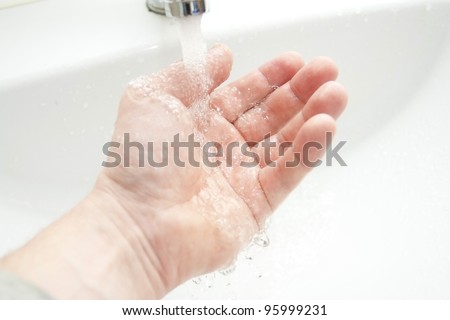 Washing of hands under the crane with water against a white washstand