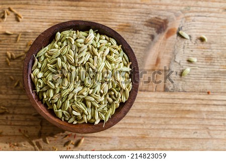 Fennel seeds in a small wooden bowl on an old wooden table.