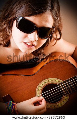 Young girl playing acoustic guitar wearing sunglasses. Portrait orientation.