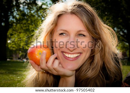 An apple a day keeps the doctor away. Beautiful young woman about to eat an apple outdoors.