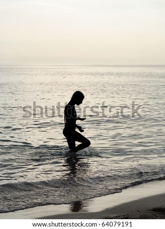 Silhouette of young little girl searching something in the sea