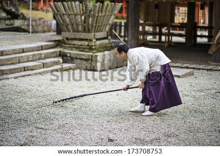 NARA, JAPAN - NOVEMBER 18, 2012: A Shinto Priest rakes a gravel Zen Garden at Kasuga-Taisha Shrine. The gardens have a long history in Japan and the surroundings are used to aid meditation.