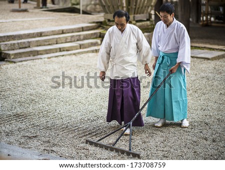 NARA, JAPAN - NOVEMBER 18, 2012: A Shinto Priest rakes a gravel Zen Garden at Kasuga-Taisha Shrine. The gardens have a long history in Japan and the surroundings are used to aid meditation.