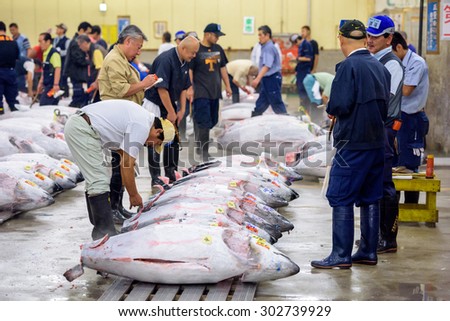 TOKYO, JAPAN - AUGUST 1, 2015: Prospective buyers inspect tuna displayed at Tsukiji Market. Tsukiji is considered the world\'s largest fish market.