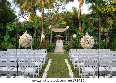 A flower bouquet with roses in front of rows of chairs at a wedding ceremony