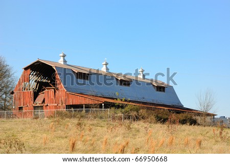 An old barn with a collapsed wall across an empty field