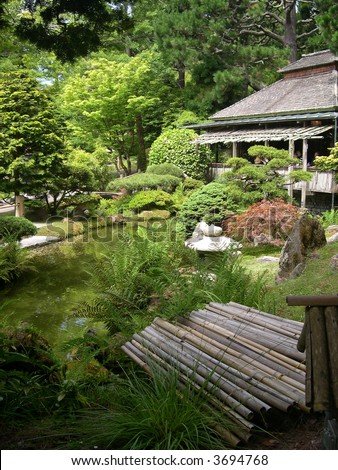 Sunny day in a beautiful Japanese garden with tea house overlooking a pond.