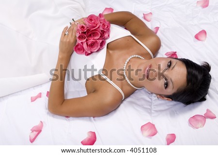 Bridal portrait laying back on white comforter with flower pedals