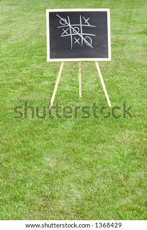 A chalkboard with tic-tac-toe game standing on the lawn. Space for copy.