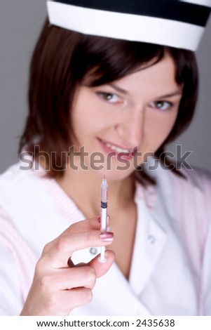 Young nurse wearing cap with syringe. Focus on the syringe