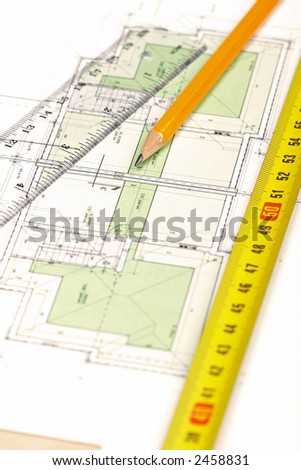 Pencil, tape measure and a ruler on top of a floor plan; Shallow depth of field with focus on pencil\'s tip.