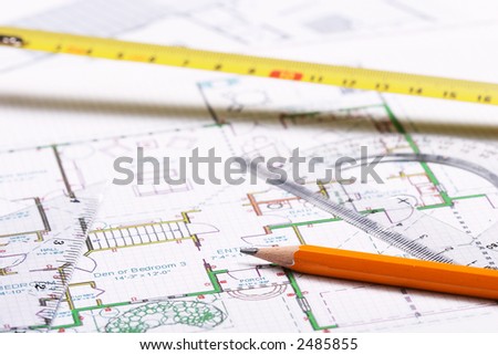 Pencil, protractor, tape measure and set square on top of floor plan. Focus on pencil\'s tip.