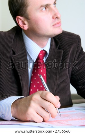 Young businessman filling up documents; focus on the person\'s hand and tip of the pen.