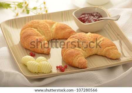 Golden flaky croissants with butter curls and strawberry red currant jam.  Selective focus on tip of foremost croissant.