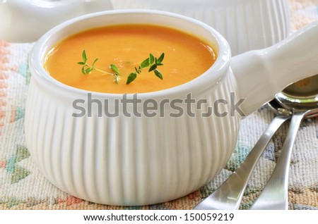 Creamy carrot and sweet potato soup with sprig of thyme in white ribbed soup bowl