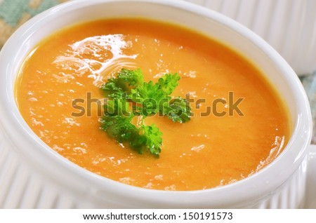 Creamy carrot and sweet potato soup with parley garnish in white ribbed soup bowl