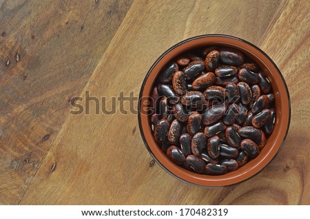 Dried Scarlet runner beans in brown dish on rustic cutting board, with room for text