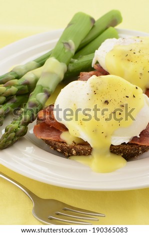 Eggs Benedict with hollandaise sauce on hearty multigrain toast with Canadian bacon and asparagus