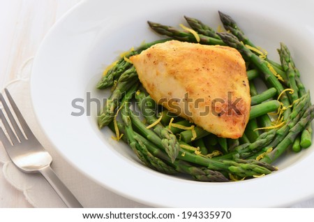 Fresh, light and healthy dinner of skinless chicken breast and tender young asparagus spears with a lemon garnish