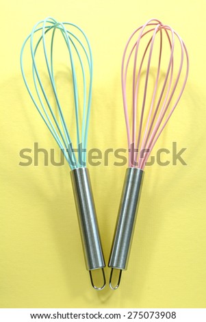 Trendy turquoise and pink kitchen whisks on sunny yellow background in vertical format