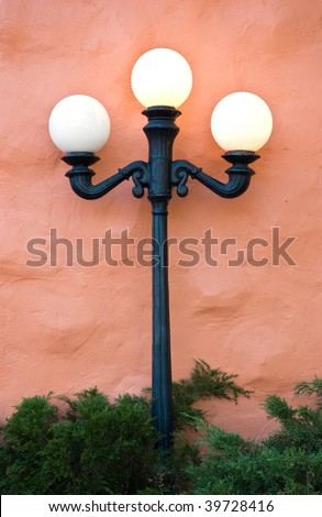 Old fashioned light fixture with three globe lights against pink adobe wall