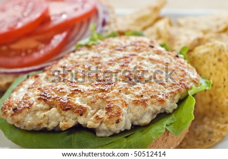 Cooked turkey cutlet on whole wheat kaiser bun with tomato and tortilla chips