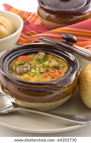 Hearty beef stew in glazed dish with bread roll, vertical format
