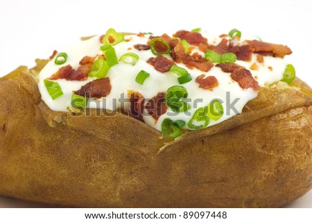 Baked russet potato with sour cream, bacon bits and green onion closeup