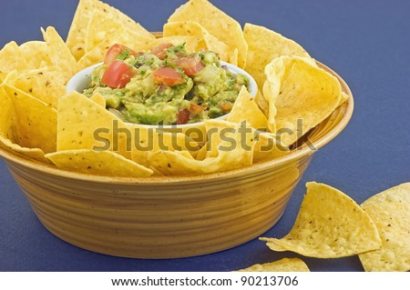 Fresh chunky Guacamole with organic corn tortilla chips on blue background