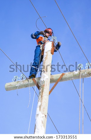 electrician working on top of an electricity pylon with the use of claws-manholes and belt