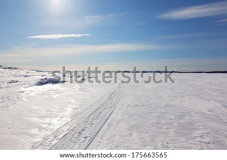 Snowmobile trail stretching into the distance against the blue sky and snowy expanses of Russia. Kandalaksha Bay of the White Sea.