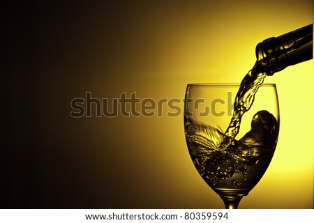 Liquid being poured into wine glass from bottle in a yellow background