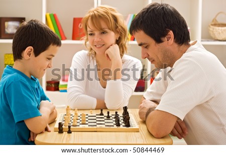 Father and his son playing chess meantime the young beautiful woman smiling