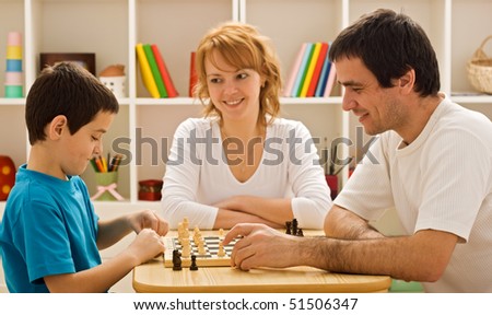 Father and his son playing chess meantime the young beautiful woman smiling