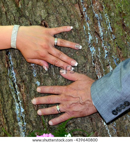 Wedding Rings in the hands of groom and bride resting against a tree.