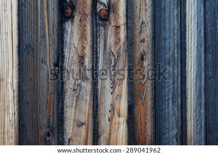Close-up view of rough textured wood plank fence. Wood panels show various colors and stages of weathering, from darker, medium browns to light colored sections. Horizontal background image.