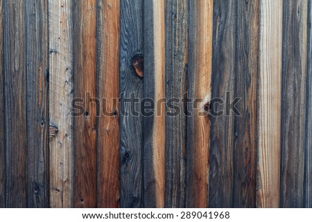 Rough textured wood plank fence. Wood panels show various colors and stages of weathering, from darker, medium browns to light colored sections. Horizontal background image.