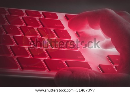 Hand on a keyboard with red lighting signifying danger, adult or off limits online use, e.g. hacking, fraud, online scams or hacker activity