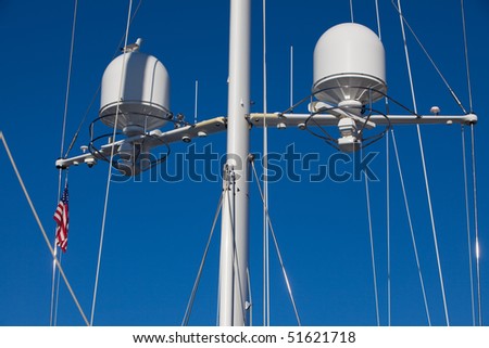 Main mast from a luxury yacht against the blue sky. The mast features two radars and rigging