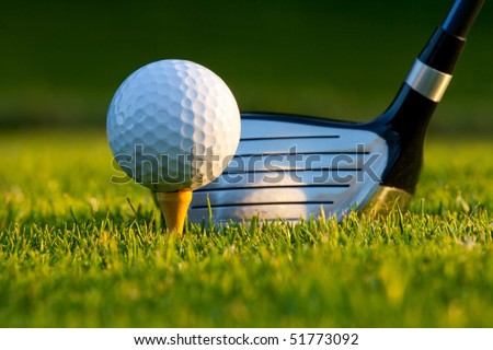 Golf ball on tee in front of driver on a gold course