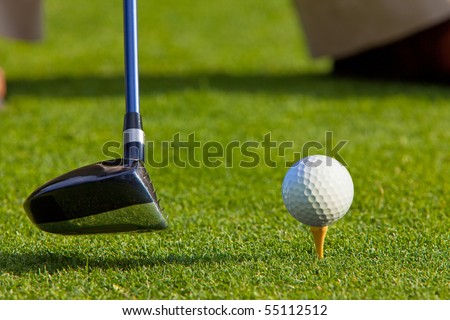 Close up of golf ball on a tee with the driver positioned ready to hit the ball. The golfer’s feet and shoes are partially visible in the background.