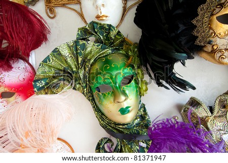 A variety of colorful Venetian carnival masks with ornate decorations;  a green mask is located in the center of the photo