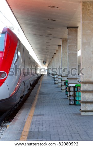 Modern high speed European train parked at a covered and empty platform in a typical, small to medium sized train station in Italy.