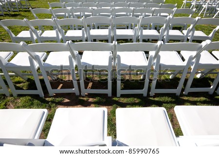 Organized rows of white, wooden chairs neatly arranged for an outdoor ceremony or event like a wedding, concert, commencement, graduation, play or speech.