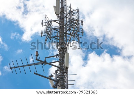 Electronic communications and cell phone tower under partially cloudy sky. Horizontal format