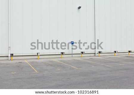 Empty parking lot with enumerated parking spots and parking sign in front of white wall