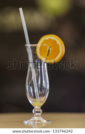 Empty hurricane glass with remains of freshly squeezed orange juice with the decorative orange slice and a straw