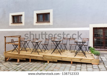 Empty restaurant or coffee shop terrace with wooden and metallic chairs and tables on the wooden platform in front of the pink wall on the street  covered with granite tiles